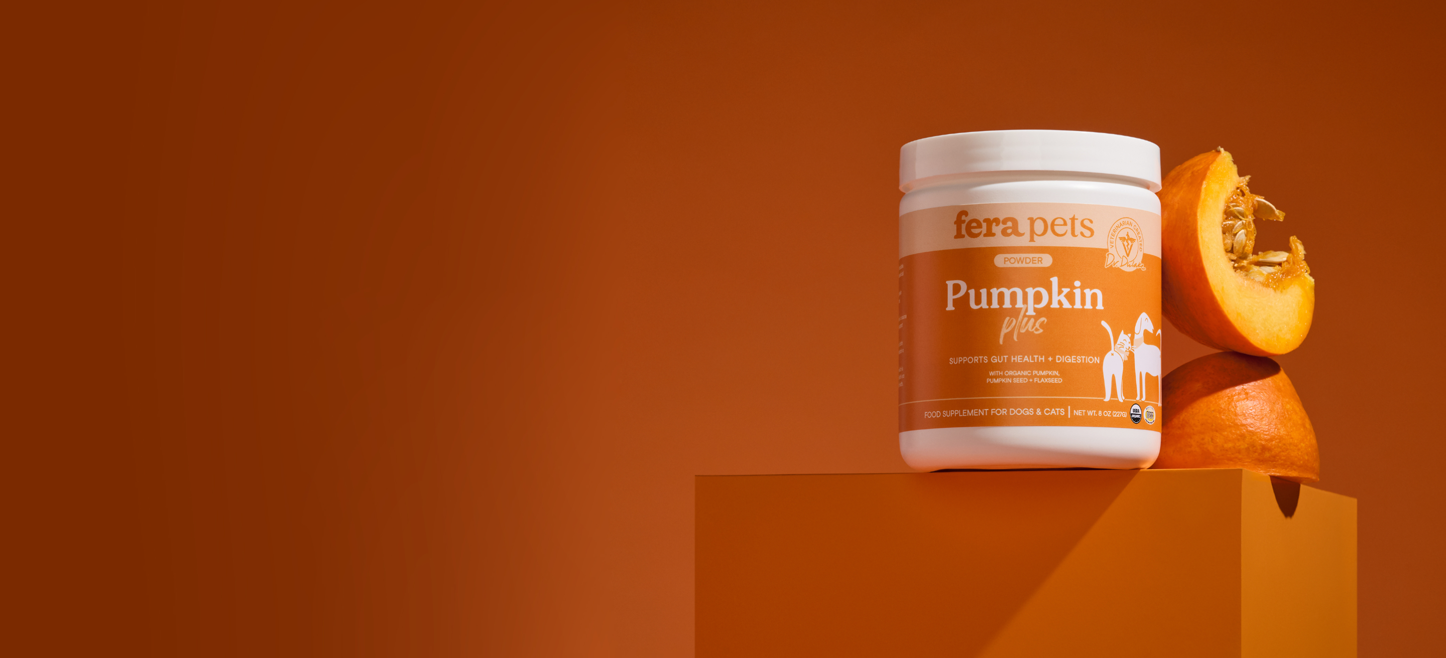 A white tub of fera pets Pumpkin Plus pet supplement sits on a matching orange pedestal next to fresh pumpkin halves, set against a solid orange background.