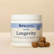 A white jar of fera pets Longevity Soft Chews for dogs, shown on a warm beige background with several brown chew pieces placed in front of the jar.